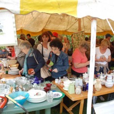 Bric_a_brac stall, crowded. Hazel Rendle, right, and Anella Parker Martin, pointing Crowded bric a brac stall. On the left, Hazel Rendle, one of the village residents running the stall.