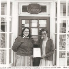 Jean Emptage with certificate and Judy Barber outside door of Post Office